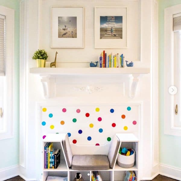 Kids Reading Nook Idea - A corner fireplace is closed off and painted all white with some fun colored polka dots. There is a bookshelf that doubles as a set for reading in front of the painted wall. 