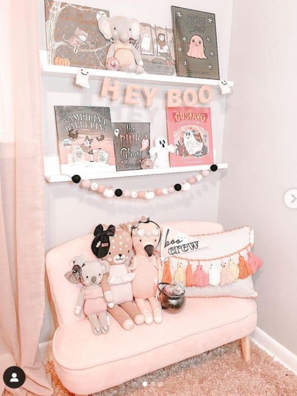 Kids Book Nook Idea - a small pink child-sized sofa sits on the ground underneath some white ledge shelves filled with books to read. 
