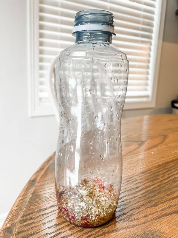 Image of plastic water bottle with about 1/2 inch of pink and gold glitter filled on the bottom. 
