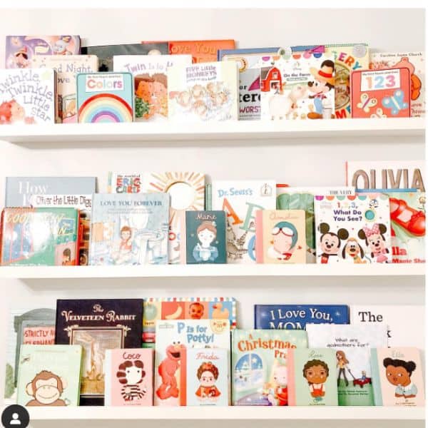 3 long white picture ledge shelves filled with books in a baby's nursery. 