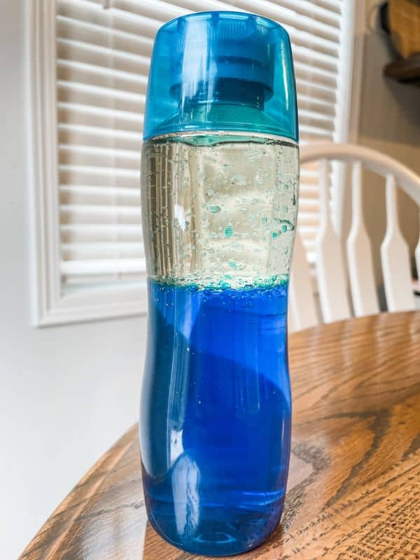 Image of the completed oil and water sensory bottle with blue water in the bottom half of the bottle and vegetable oil in the top half of the bottle. 