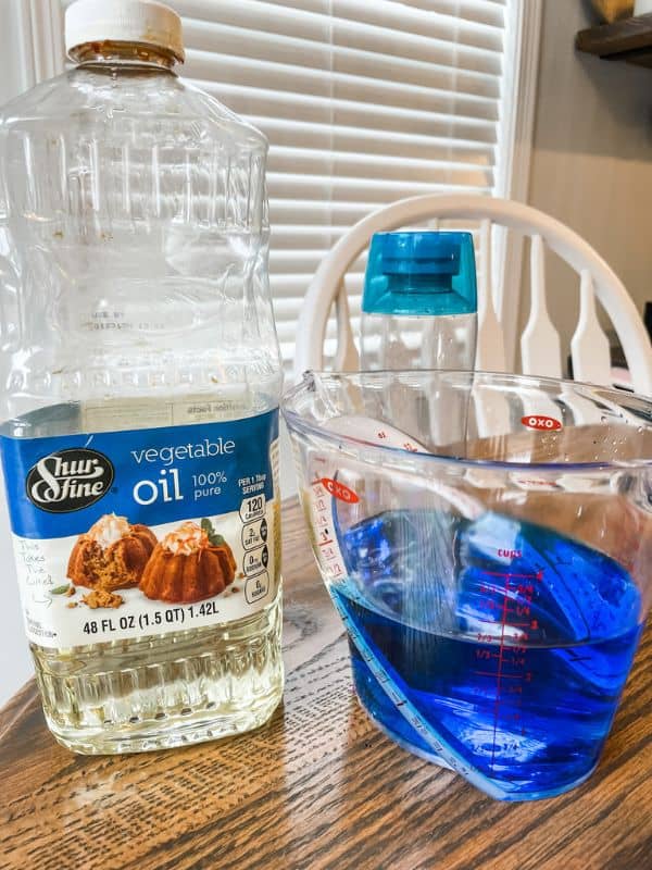 Image of the materials need for an oil and water sensory bottle. The materials and ingredients include a clear plastic bottle, vegetable oil, blue food coloring, and warm water. 