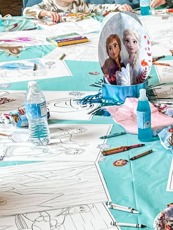 Frozen themed birthday party activities - image of the main table with a teal tablecloth on it and several large Frozen themed coloring pages and crayons for the kids to color. 