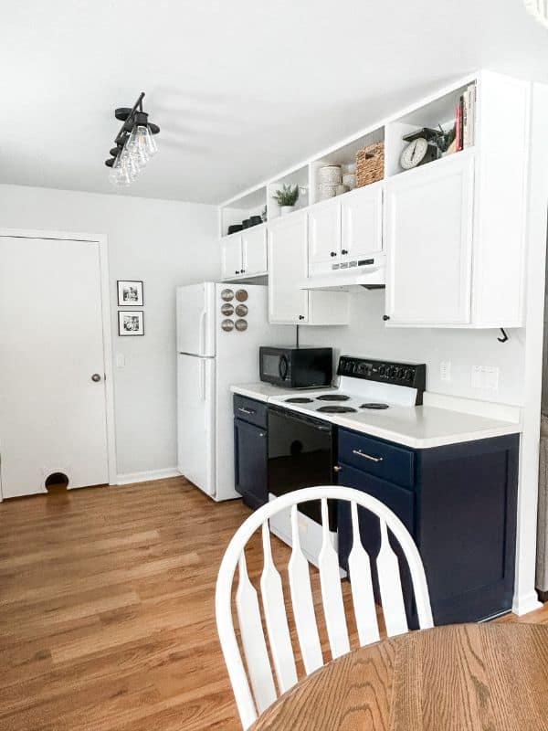 Image of the completed kitchen makeover project. The upper cabinets are painted white and stretch all the way to the ceiling. The bottom cabinets are painted navy blue. 