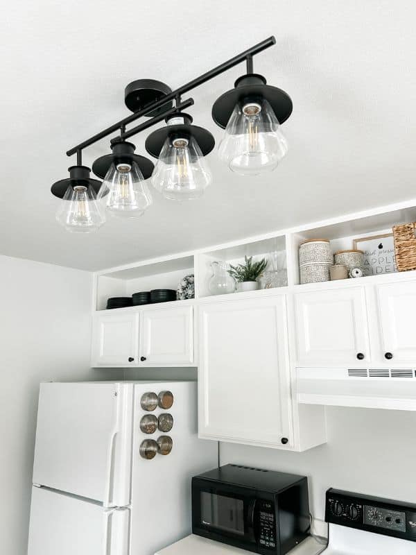 Image of the completed kitchen makeover project. The upper cabinets are painted white and stretch all the way to the ceiling with a black track light in the foreground.