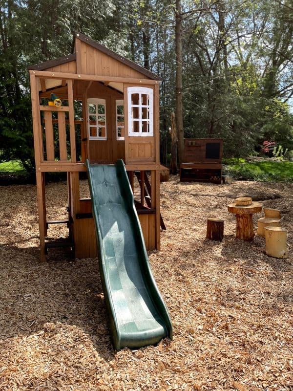 Wooden playset with slide in a natural play area outside. 