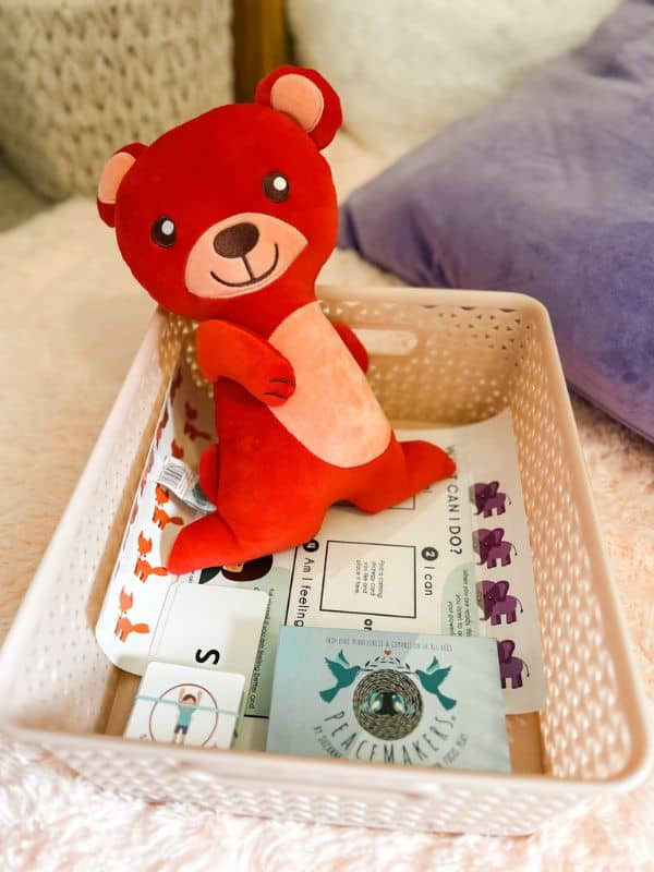 Pink basket filled with various calming corner activities and a red bear stuffed animal. 