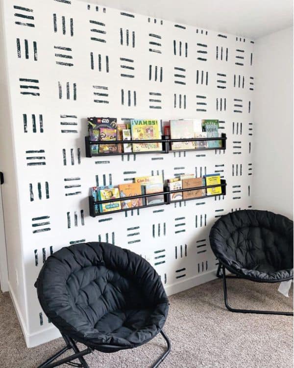 A children's reading corner with two black chairs in front of a wall with a black and white pattern.