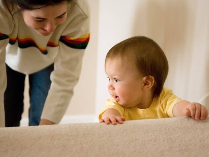 A mom follows closely behind as a baby climbs up the stairs. 