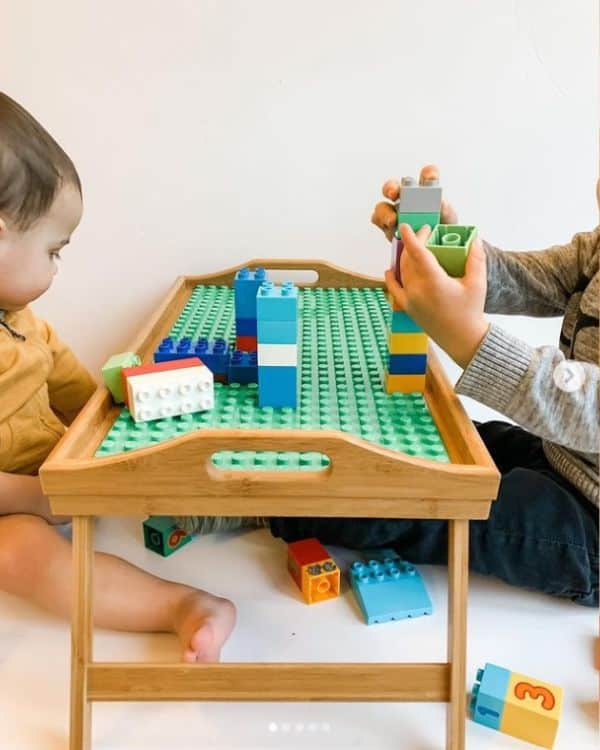 Two toddlers playing with Lego blocks on a wooden tray. 