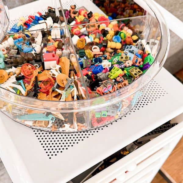 A round, divided, clear container filled with assorted small Lego parts and mini-figures.