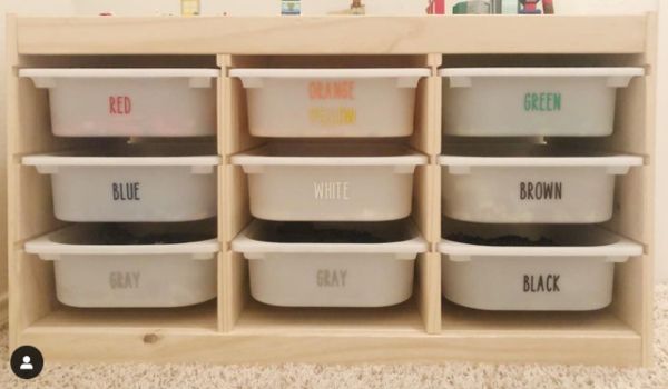 A wooden drawer unit with clear bins labeled with different colors and Lego parts categories.