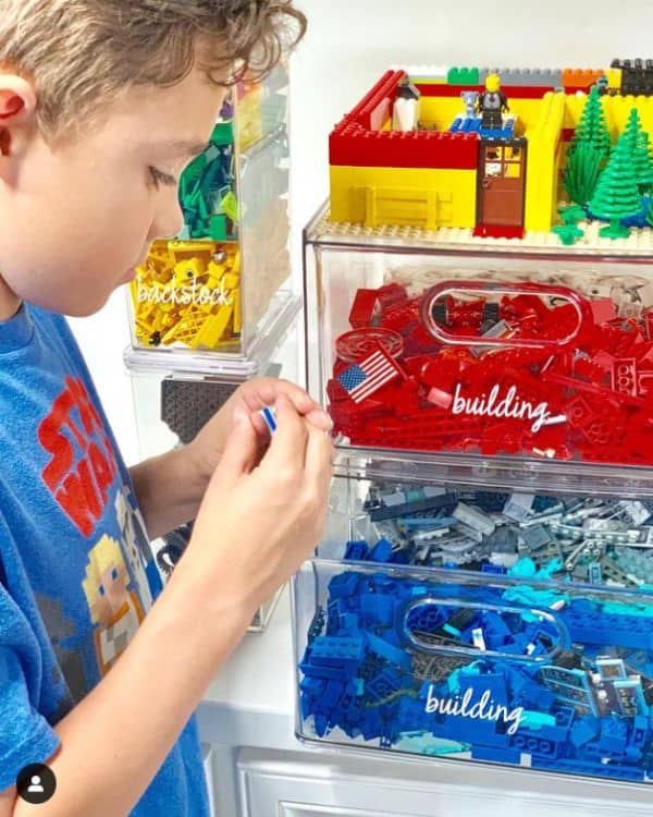  A boy sorting Lego pieces from clear plastic bins labeled 'building' and 'backstock' with a Lego creation displayed on top.