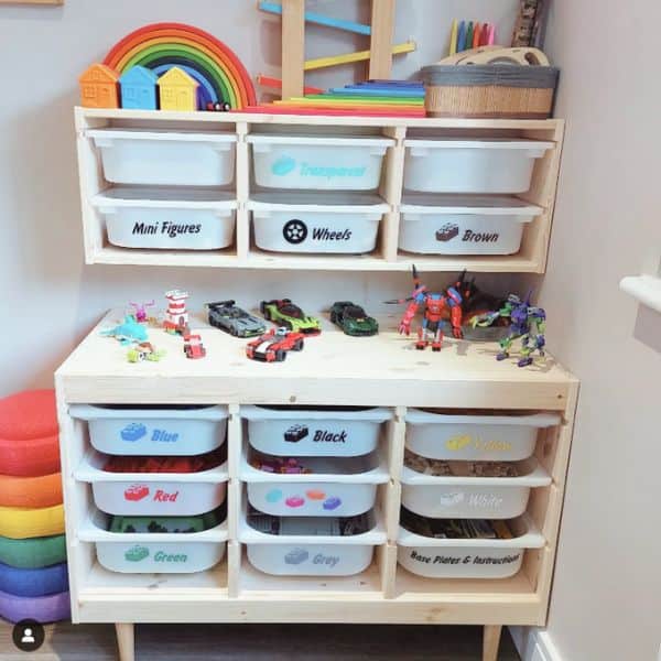 A wooden storage unit with labeled plastic bins organized by color and Lego parts like 'Mini Figures' and 'Wheels.