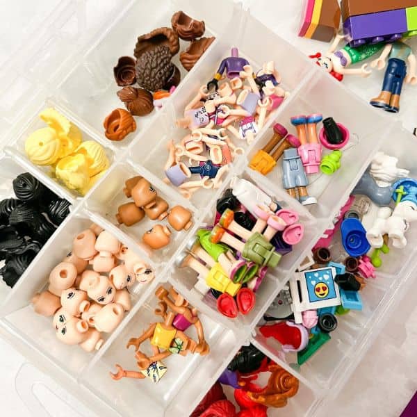 A clear compartment organizer filled with small Lego accessories and mini-figure parts.