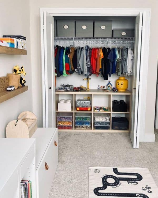 A closet organizer with clear drawers filled with sorted Lego pieces and toys, clothes hanging above.